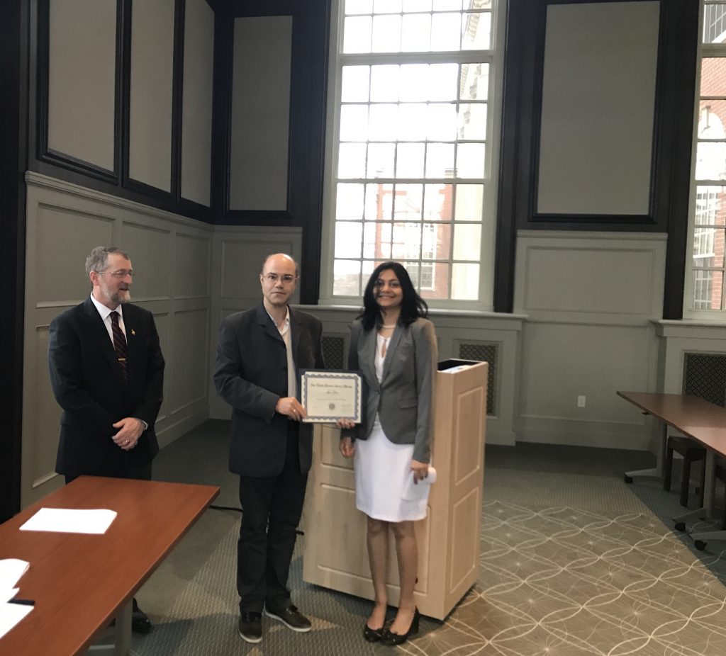Serge Nakhmanson and Ayana Ghosh standing in a large room. Prof. Nakhmanson is holding Ayana's fellowship certificate.
